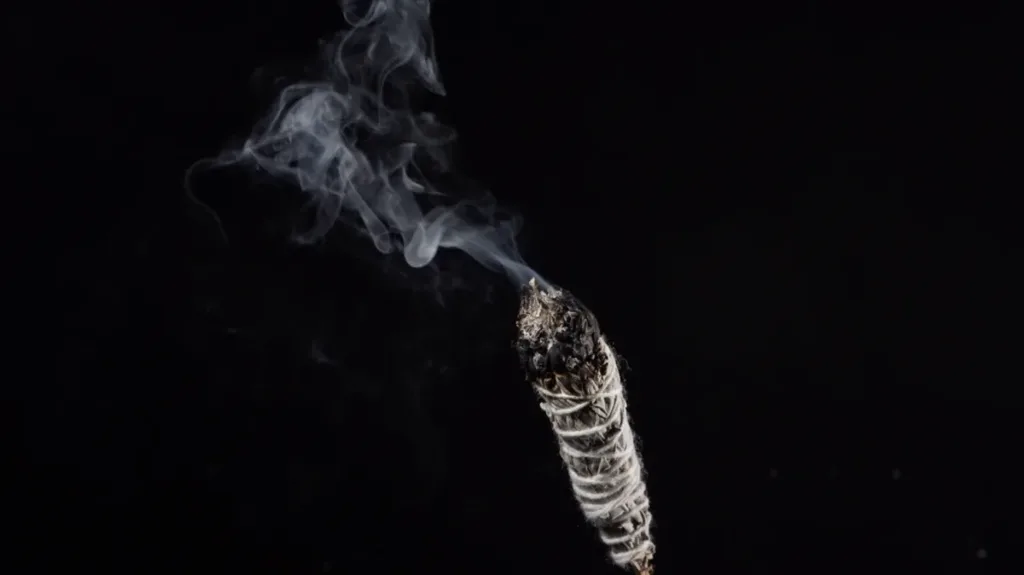 A burning sage smudge stick with rising smoke